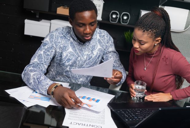Various business colleagues sitting at table in modern office talking together. An African-American businessman and entrepreneur have an informal meeting in Cabinet. Two friendly black young men understand financial documents at Desk