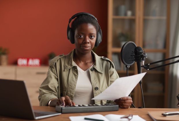 Portrait of smiling African-American woman looking at camera and wearing headphones while composing music in recording studio, copy space